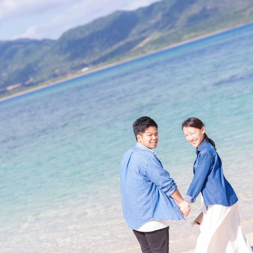 小浜島の海を背景に手を繋いで振り向く新郎新婦