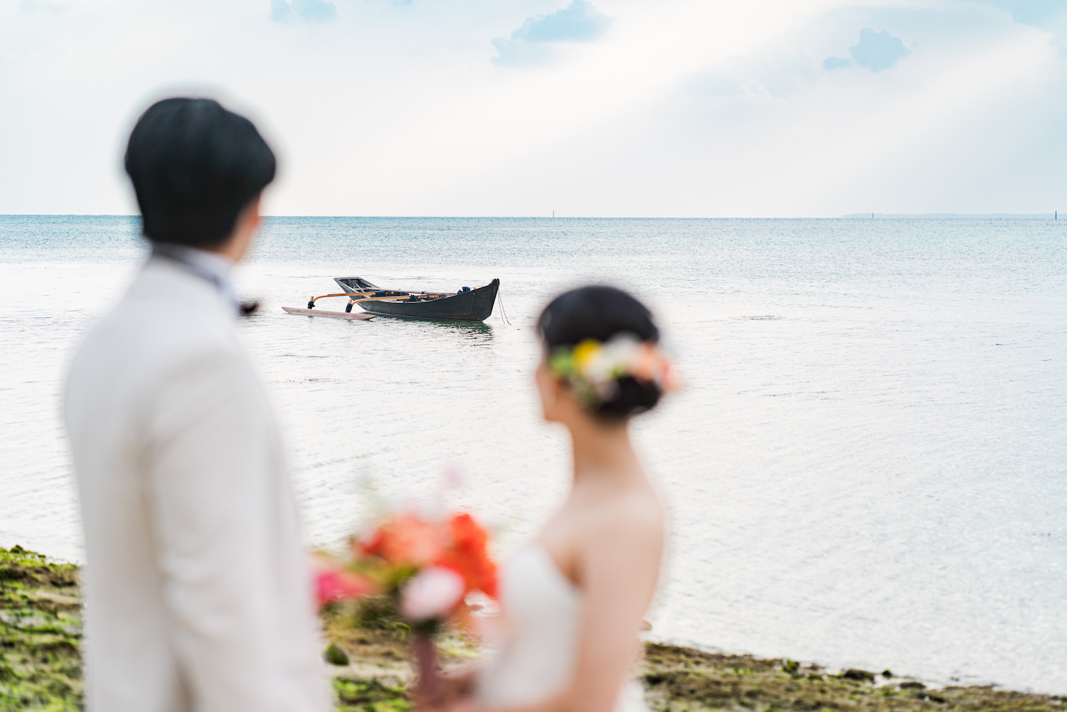 竹富島のビーチでサバニ船を眺める新郎新婦