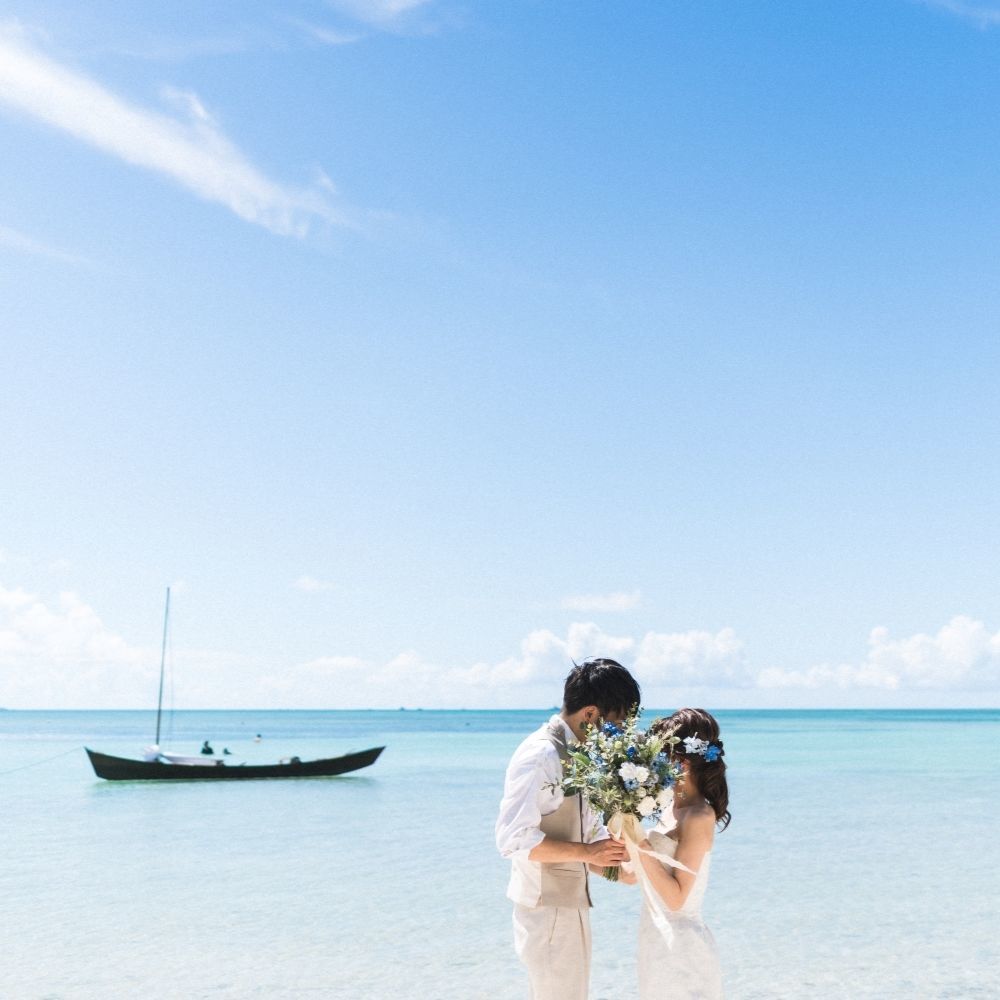 竹富島の海に浮かぶサバニ船とブーケで顔を隠す新郎新婦