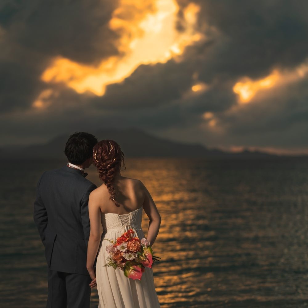 夕焼けに染まる海を眺める新郎新婦の後ろ姿
