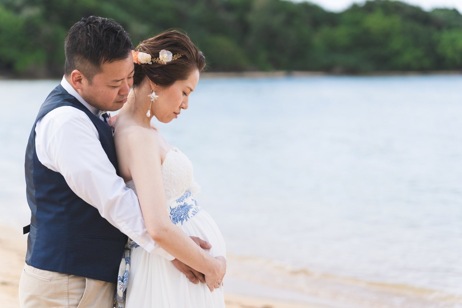 石垣島の海を背景におなかに手を添える新郎新婦