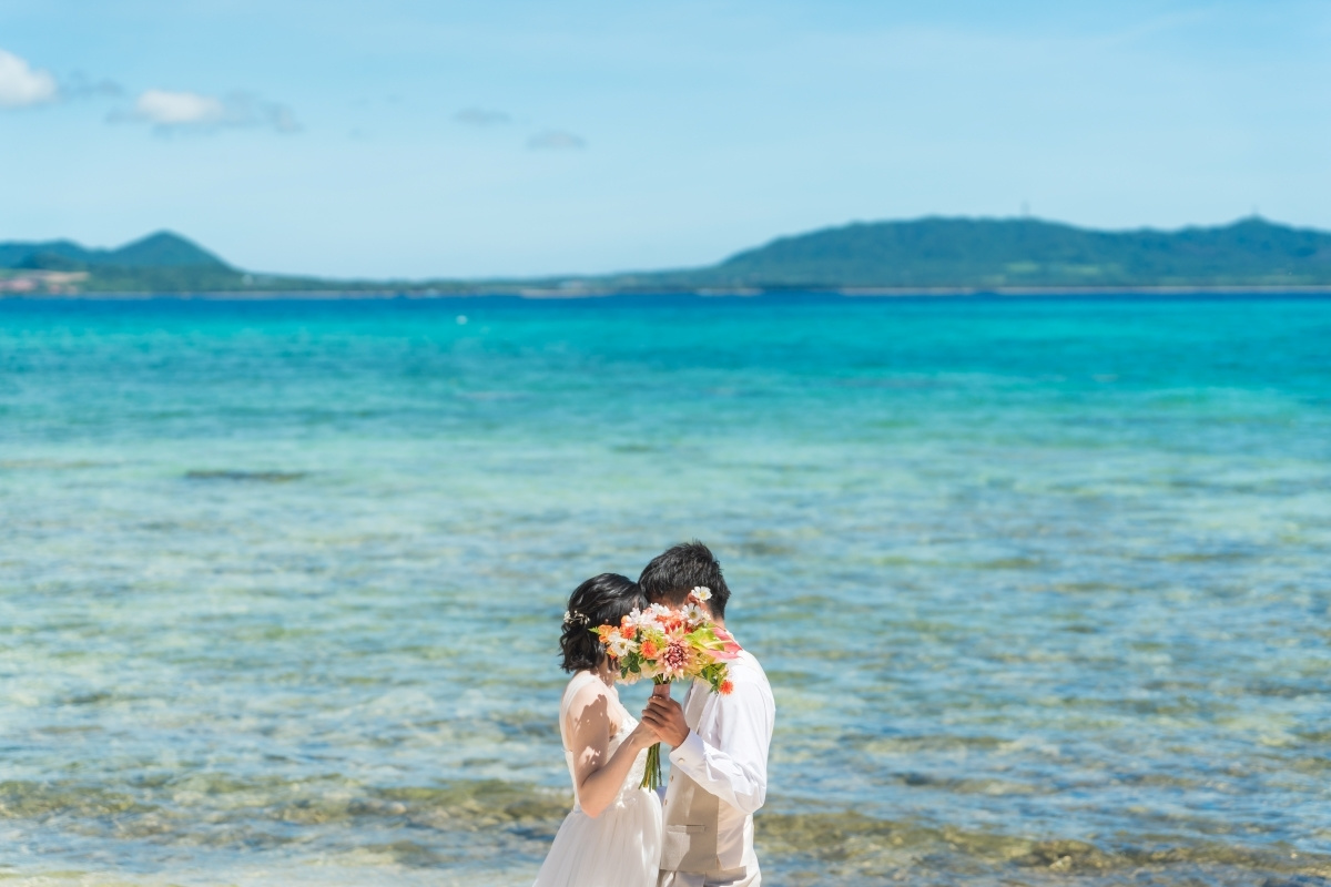 石垣島の海を背景にブーケで顔を隠す新郎新婦