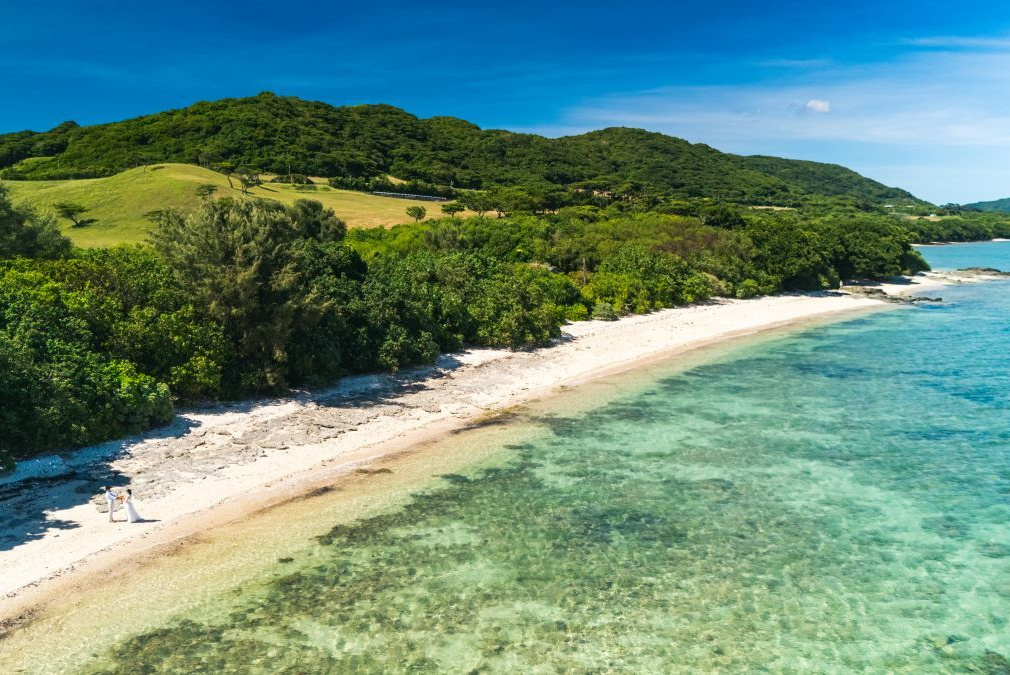 石垣島の海を背景に向かい合って顔を寄せ合う新郎新婦