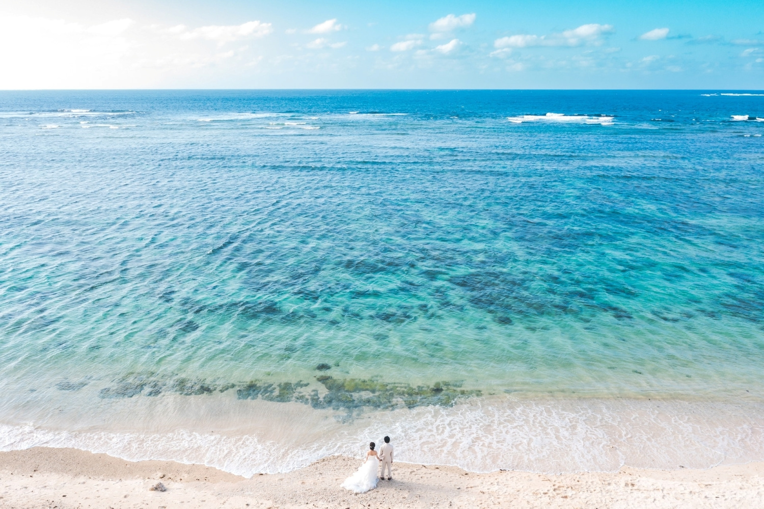 石垣島の青い海を眺める新郎新婦のドローン写真