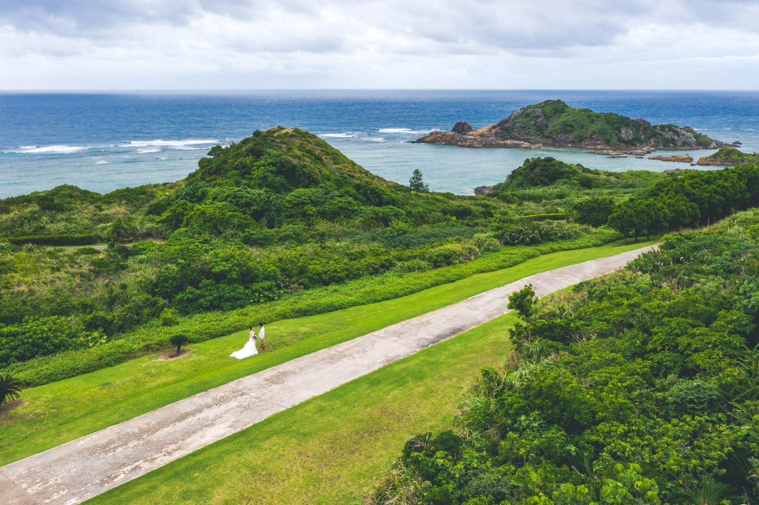 石垣島の緑に囲まれた道を歩く新郎新婦のドローン写真