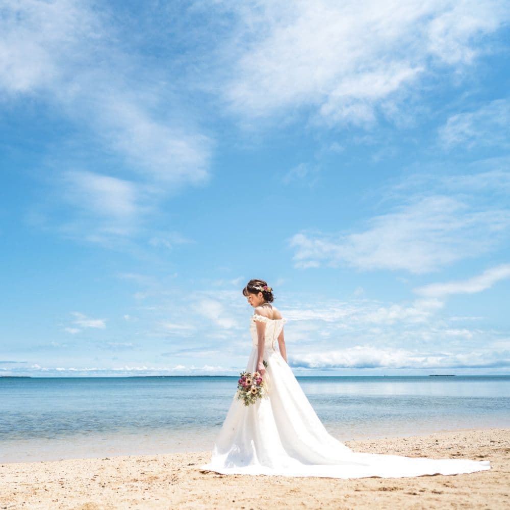 青空と青い海を背景にビーチに佇む新婦