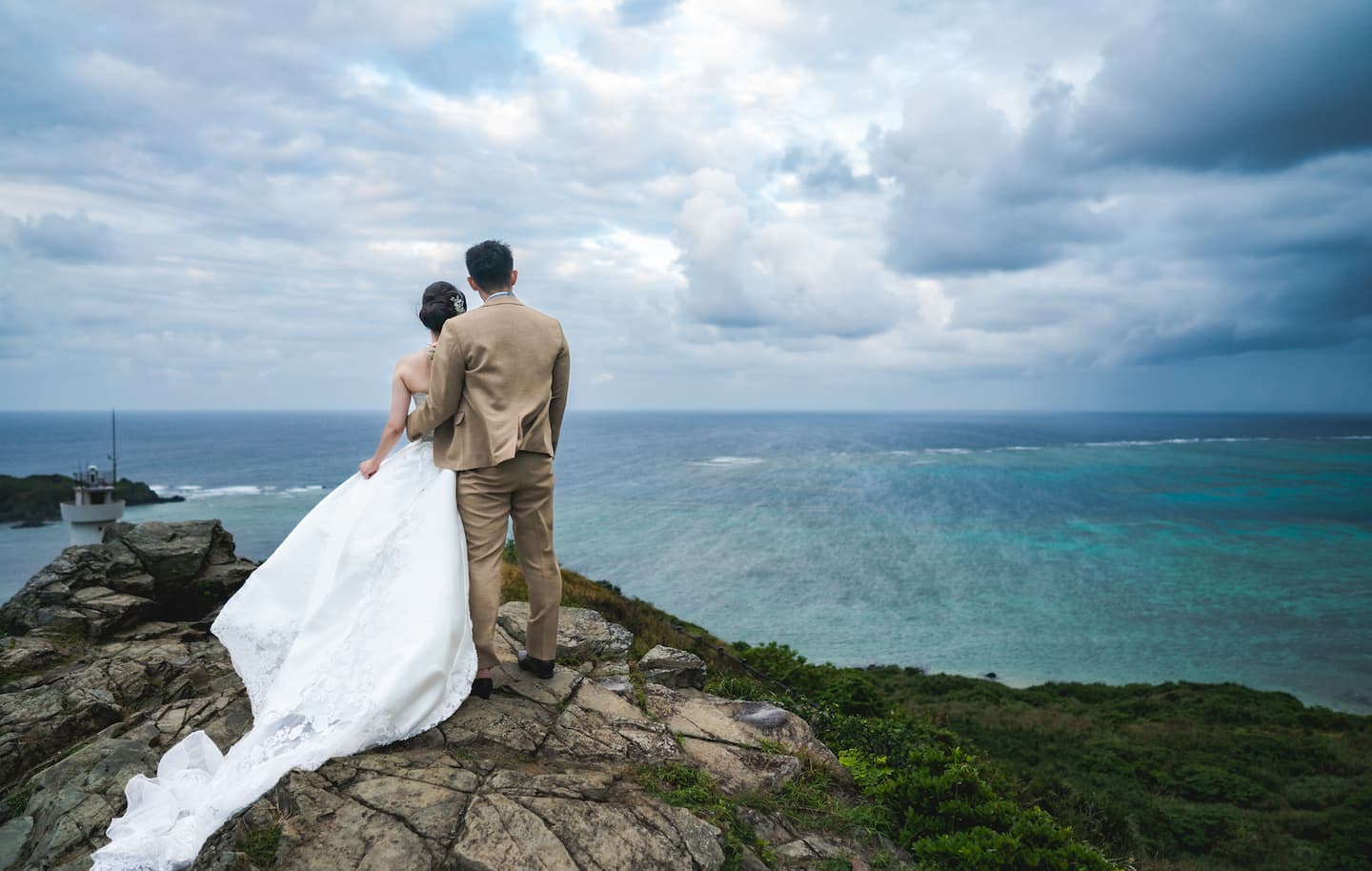 海を見渡す崖で肩を抱き合う新郎新婦の後ろ姿
