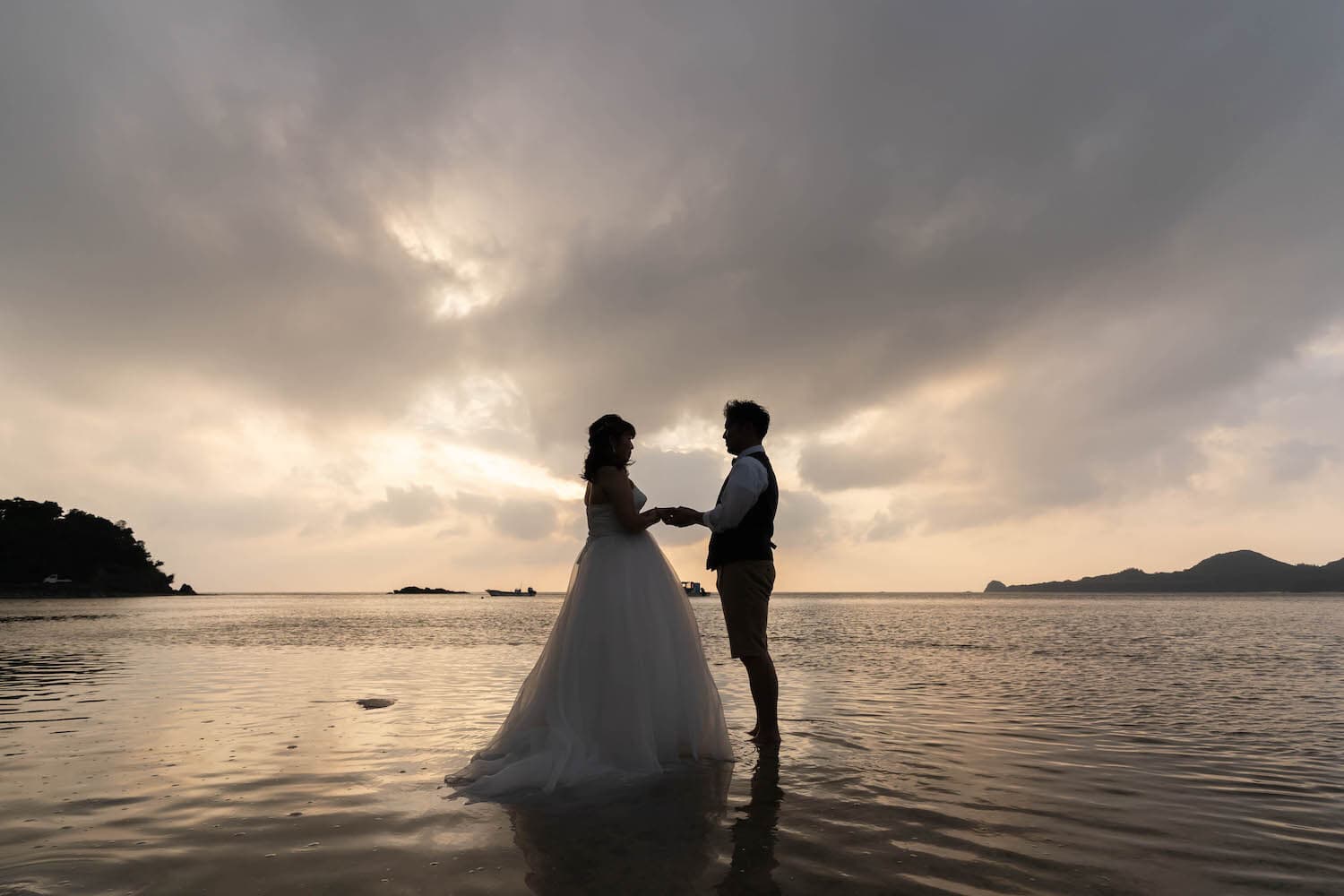 夕焼け空を背景に海で手を取り合う新郎新婦のシルエット