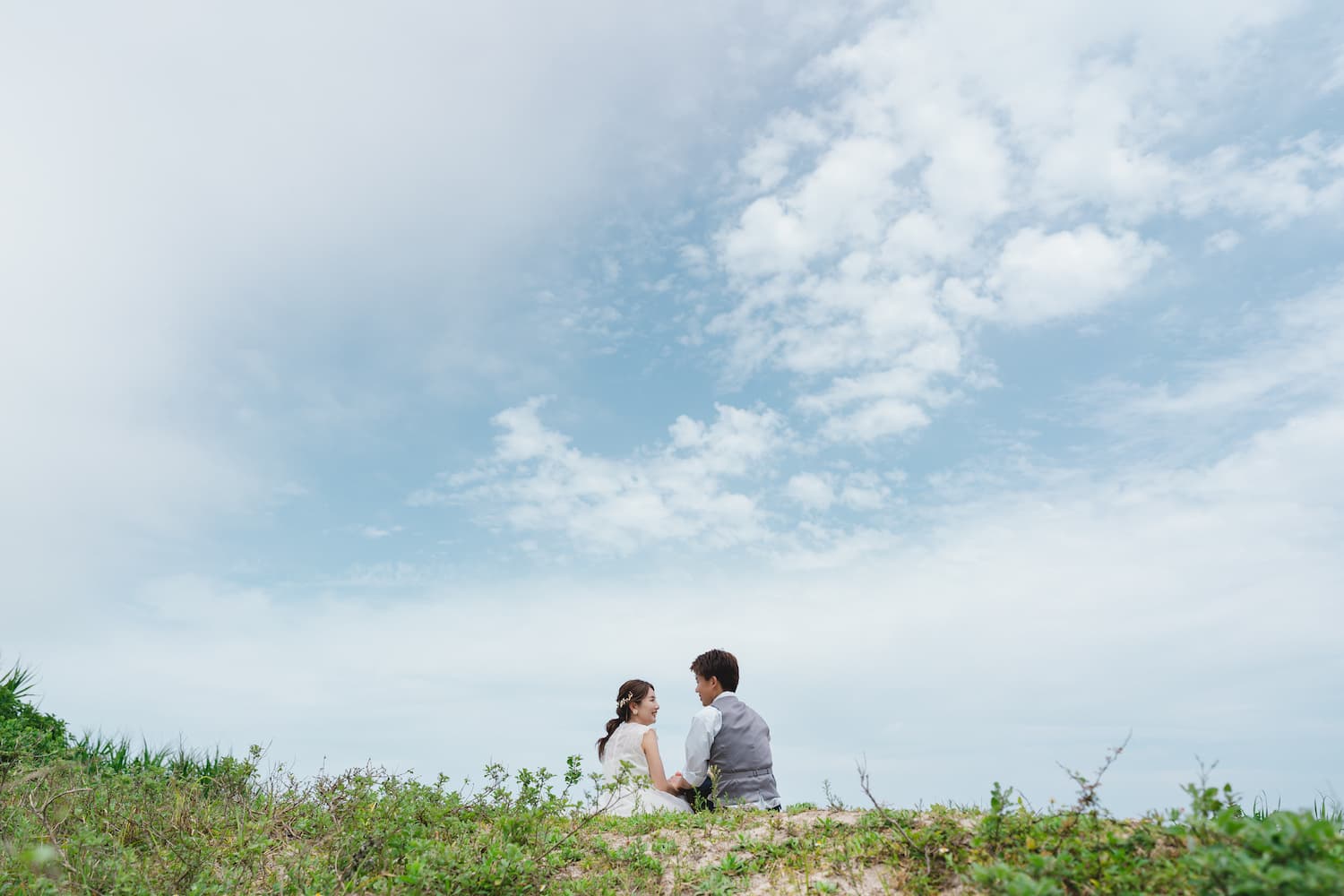 青空を背景に座って話す新郎新婦の後ろ姿