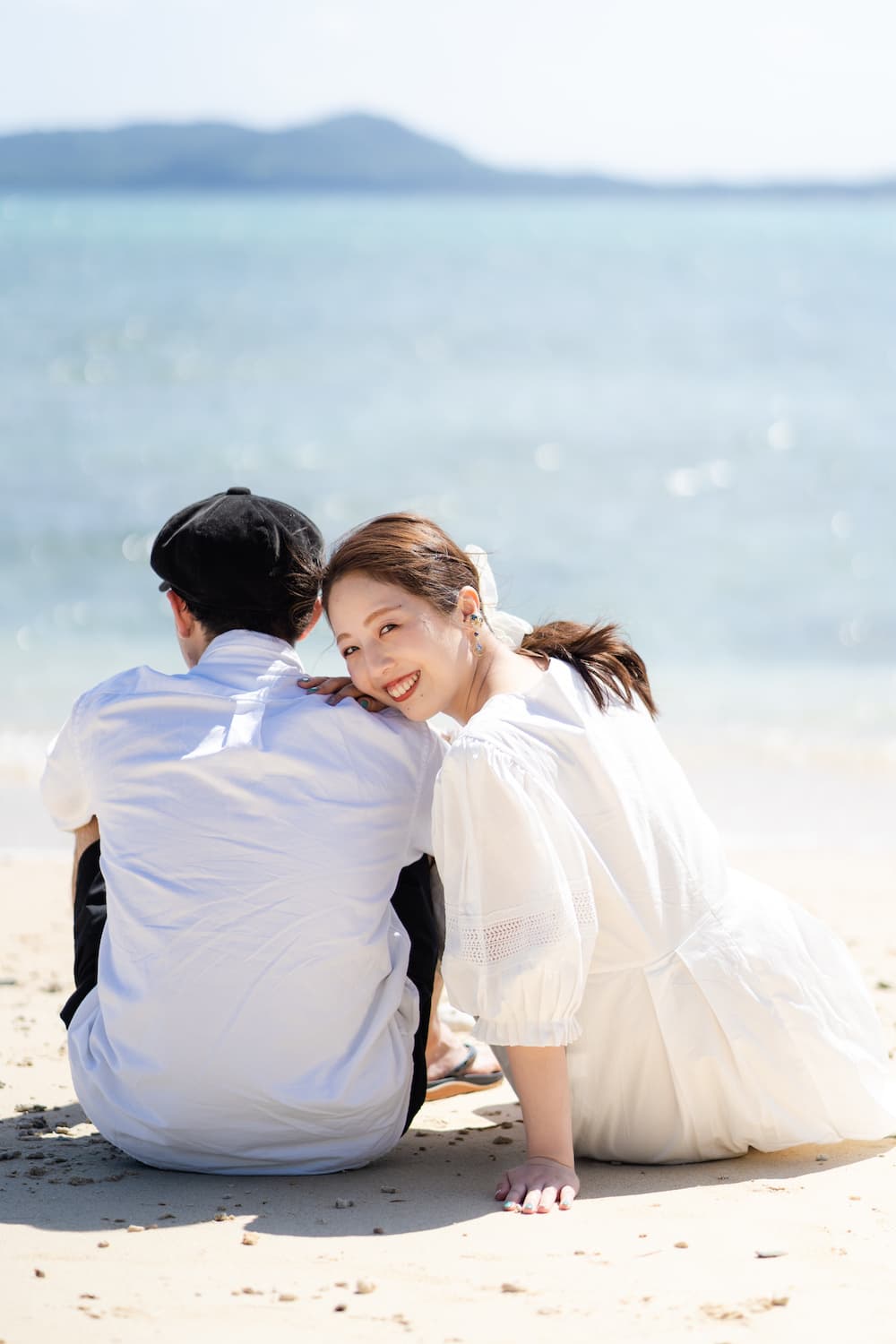 浜辺に座って新郎の肩によりかかる新婦