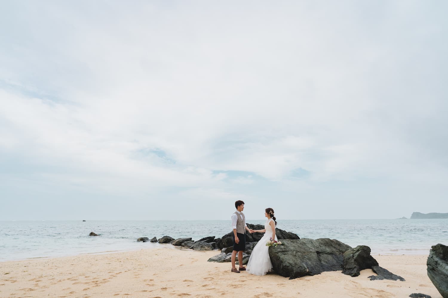 浜辺の岩場に腰をかける新婦と新郎