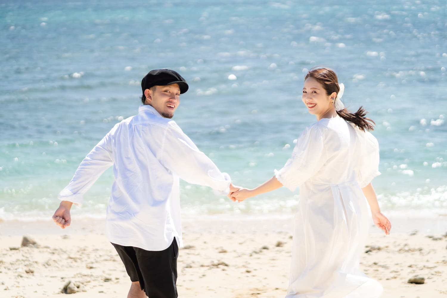 手を繋いで海へ走りながら振り向く新郎新婦