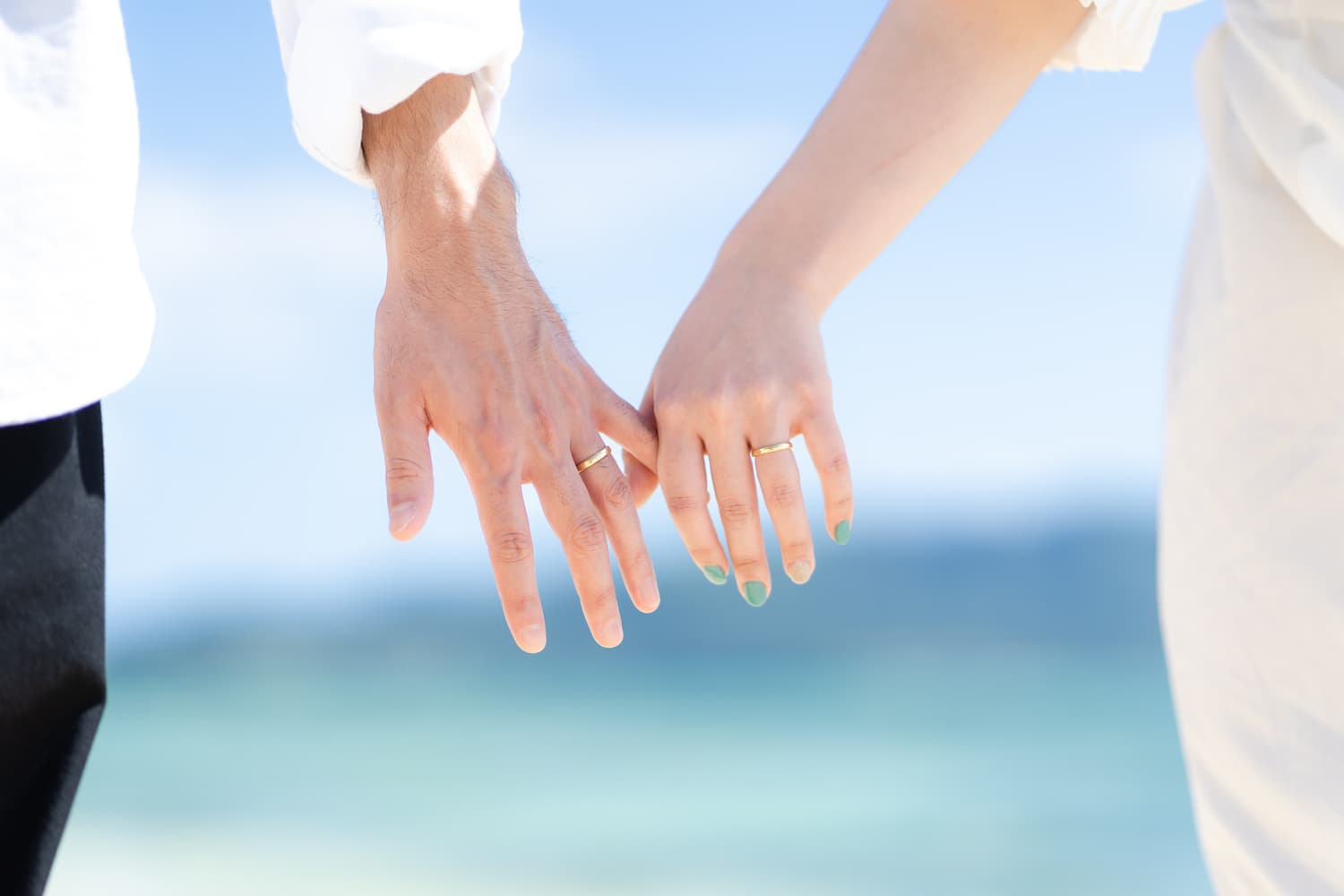 青い海を背景に指を絡ませ合う新郎新婦の手元