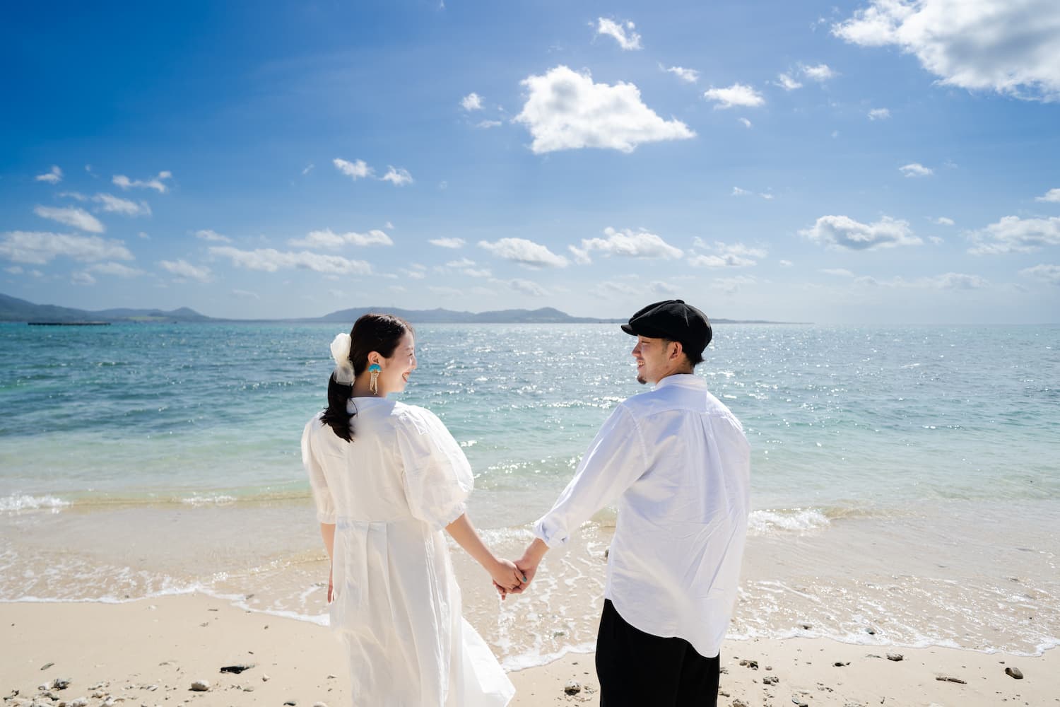 海を背景に手を繋いで微笑む新郎新婦