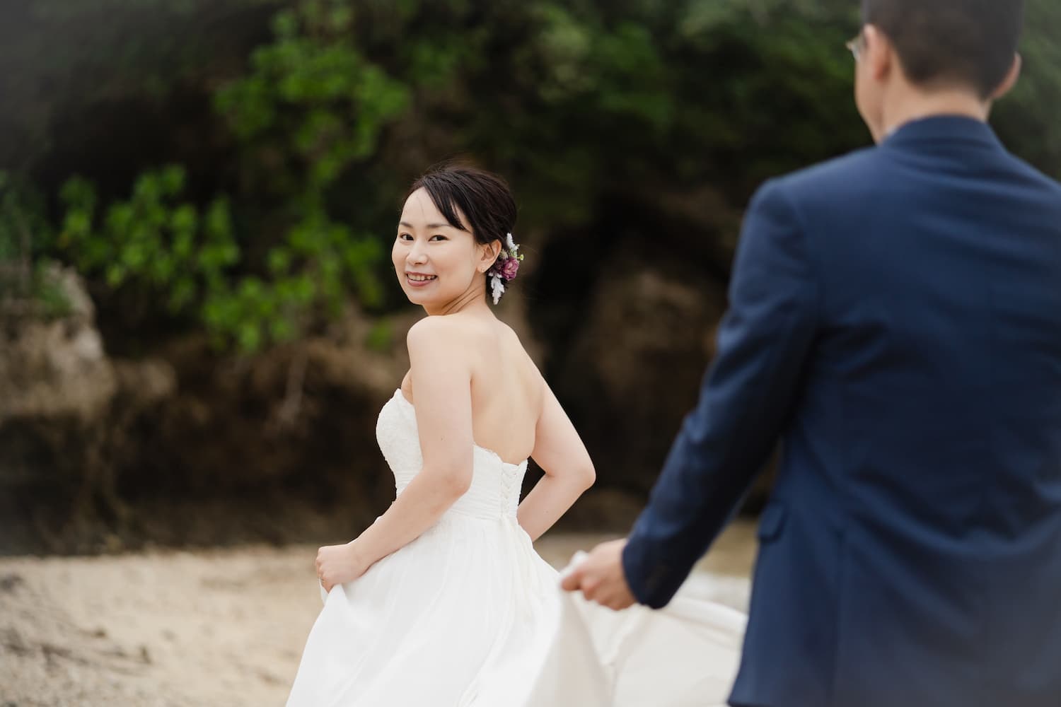 新郎にドレスの裾を持ってもらいながら浜辺を歩く新婦