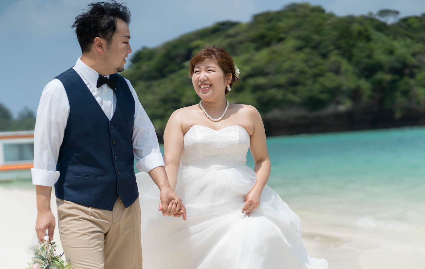 川平湾の海を背景に手を繋いで歩く新郎新婦