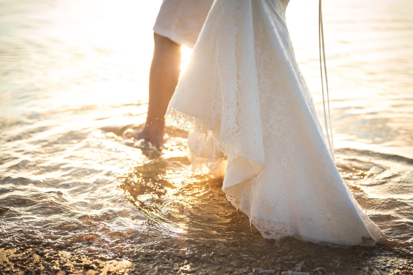 夕日に染まる海に足を踏み入れる新郎新婦の足元