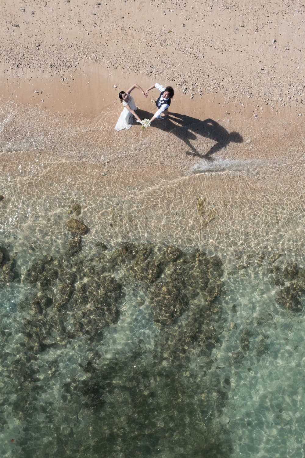 ビーチでハートマークを作る新郎新婦を頭上から写したドローン写真