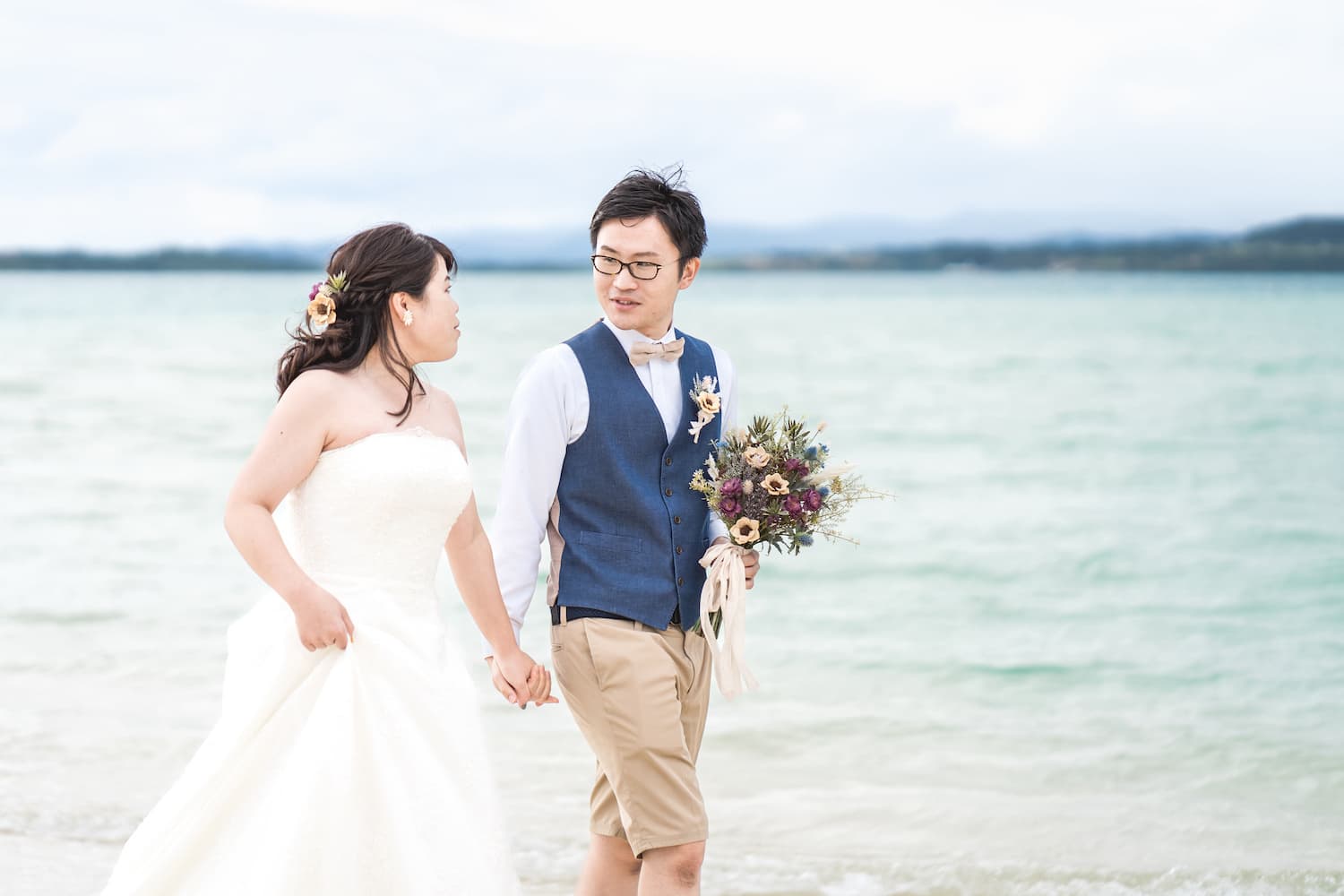 海を背景に手を繋いで見つめ合う新郎新婦