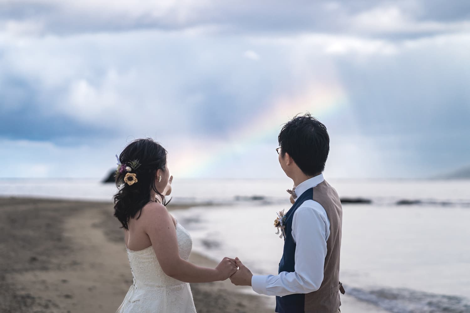 海に架かる虹を手を取り合いながら眺める新郎新婦