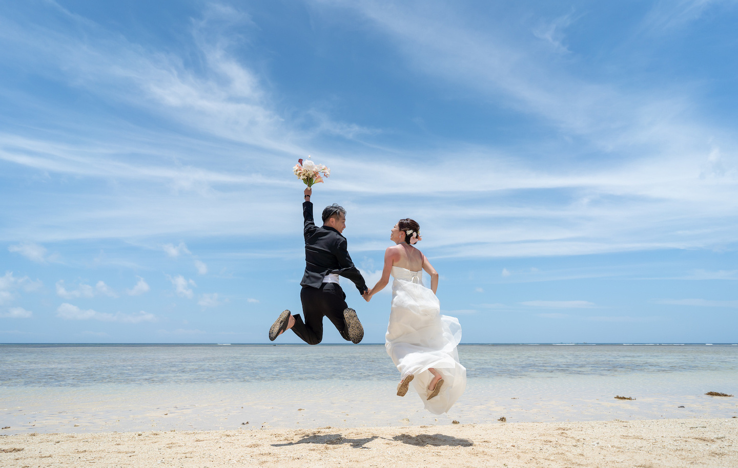 青空に向かって大きくジャンプする新郎新婦