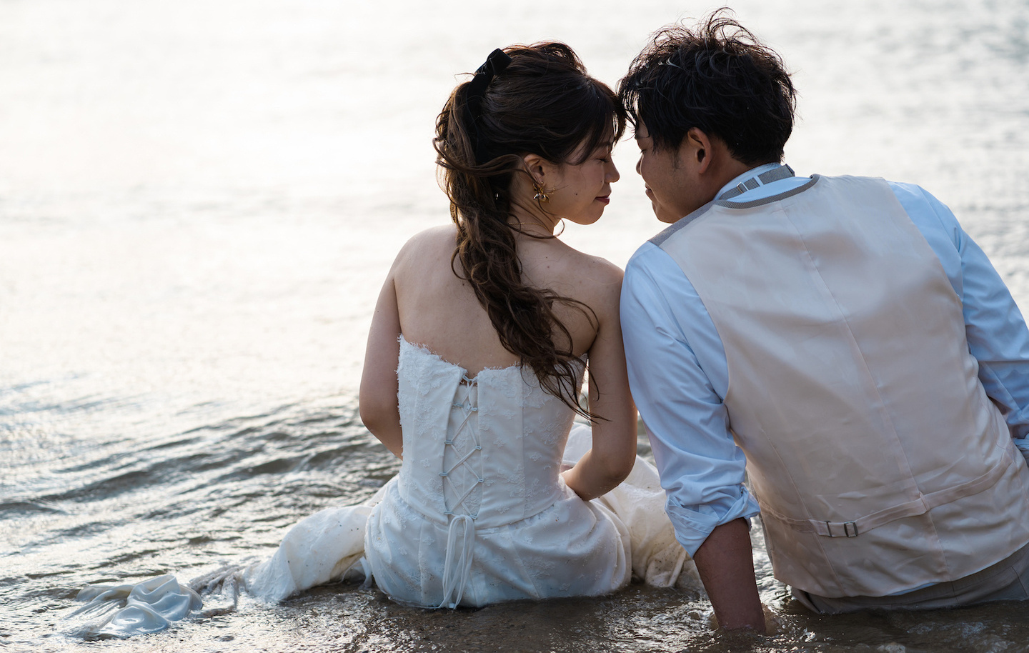 海に座って顔を寄せ合う新郎新婦