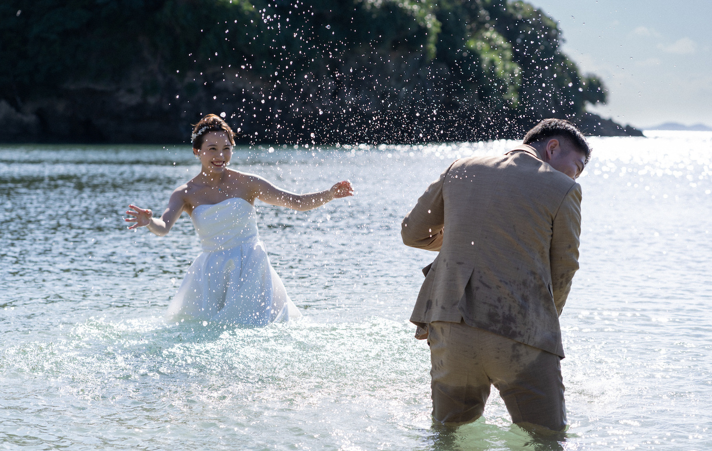 海に入って水をかけあう新郎新婦