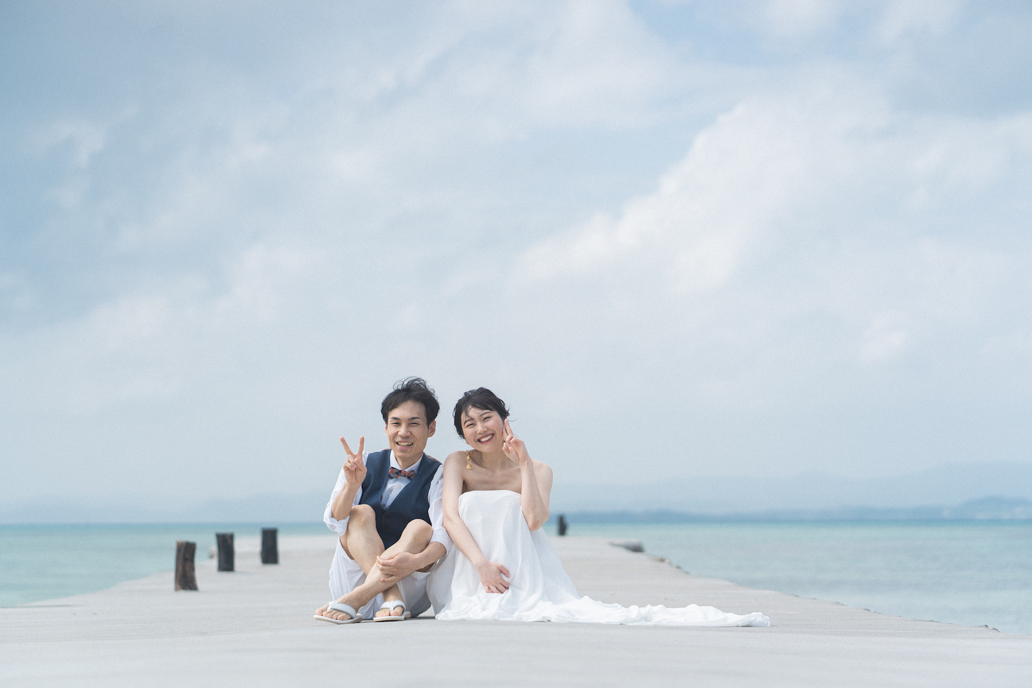 竹富島の西桟橋に座ってピースサインをする新郎新婦