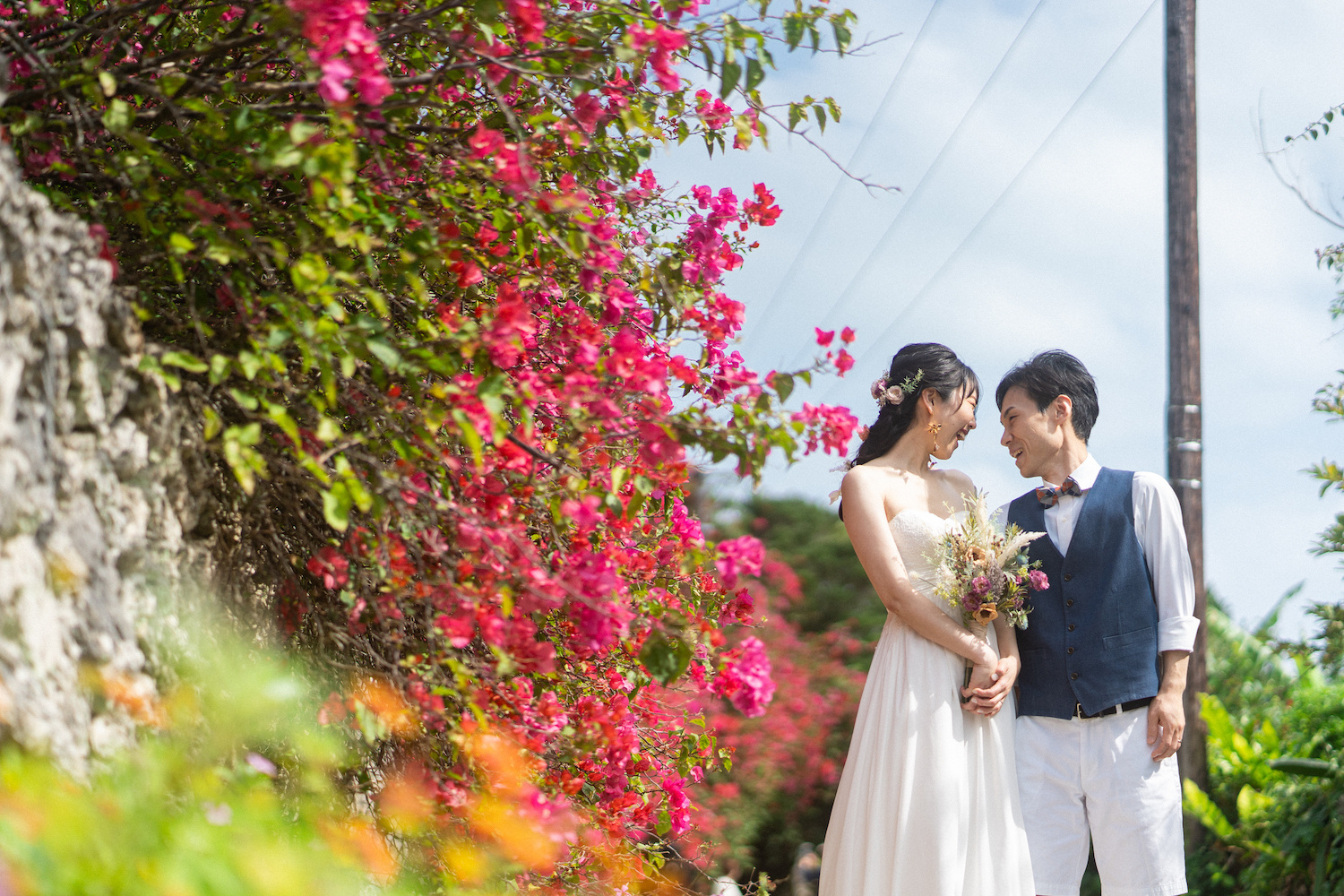 竹富島の集落にあるブーゲンビリアの前で見つめ合う新郎新婦