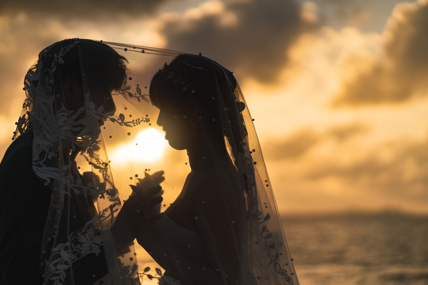 夕日に染まる海を背景に顔を寄せ合う新郎新婦のシルエット