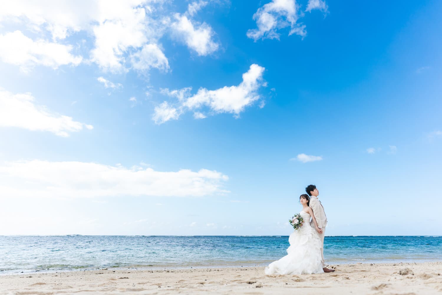 海と空を背景に背中合わせに立つ新郎新婦