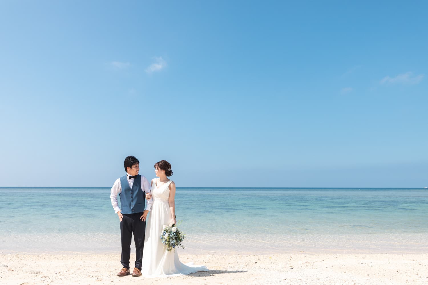 青い海と空を背景に見つめ合う新郎新婦