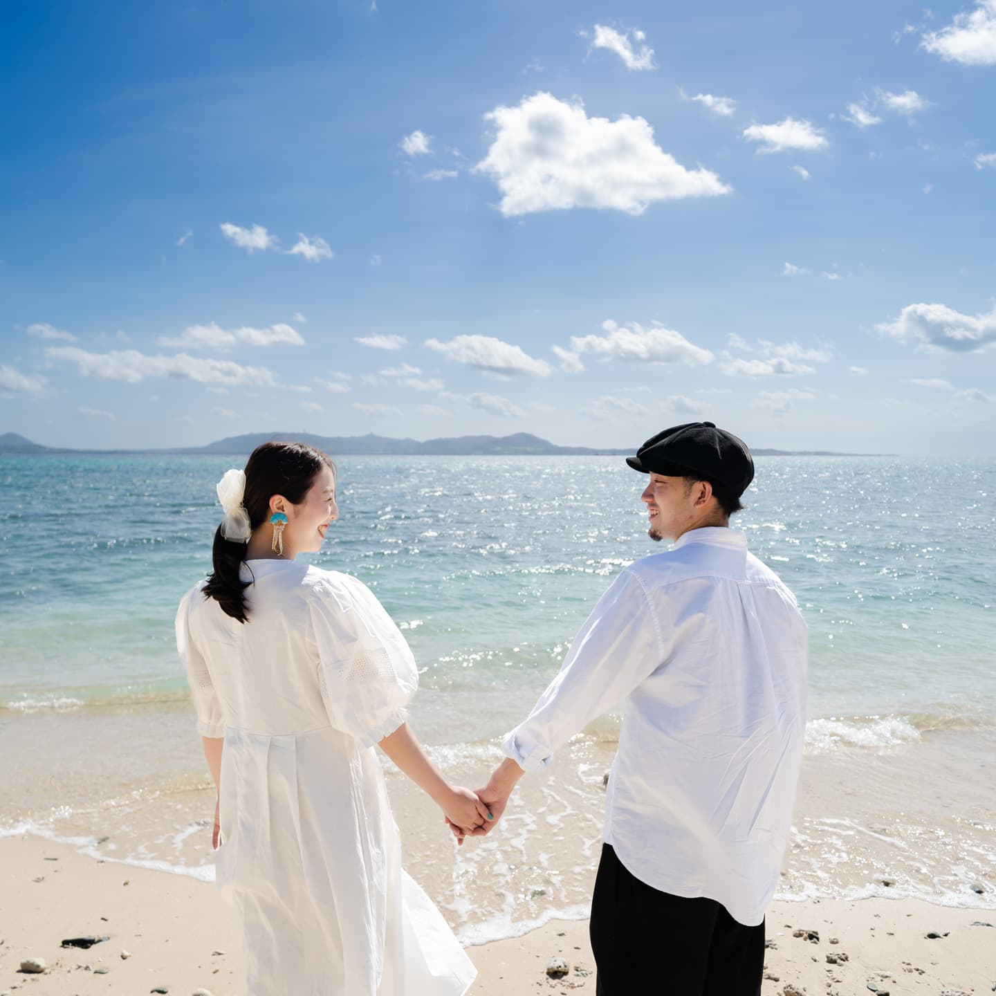 海を背景に手を繋いで見つめ合う新郎新婦