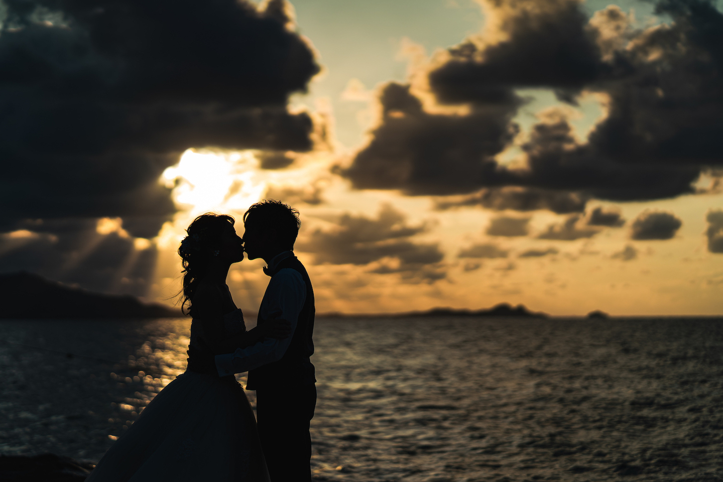 夕焼けに染まる海を背景に顔を寄せ合う新郎新婦