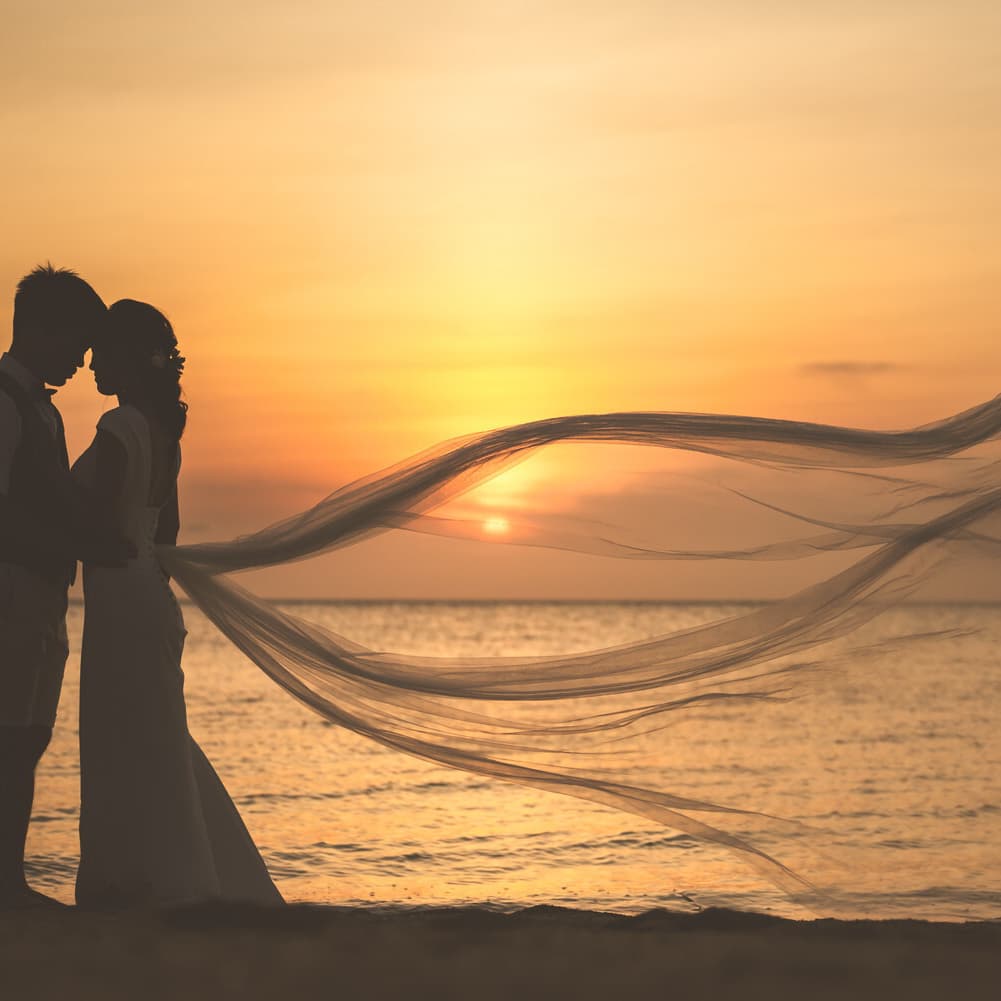 夕焼けに染まる海を背景に顔を寄せ合う新郎新婦のシルエット