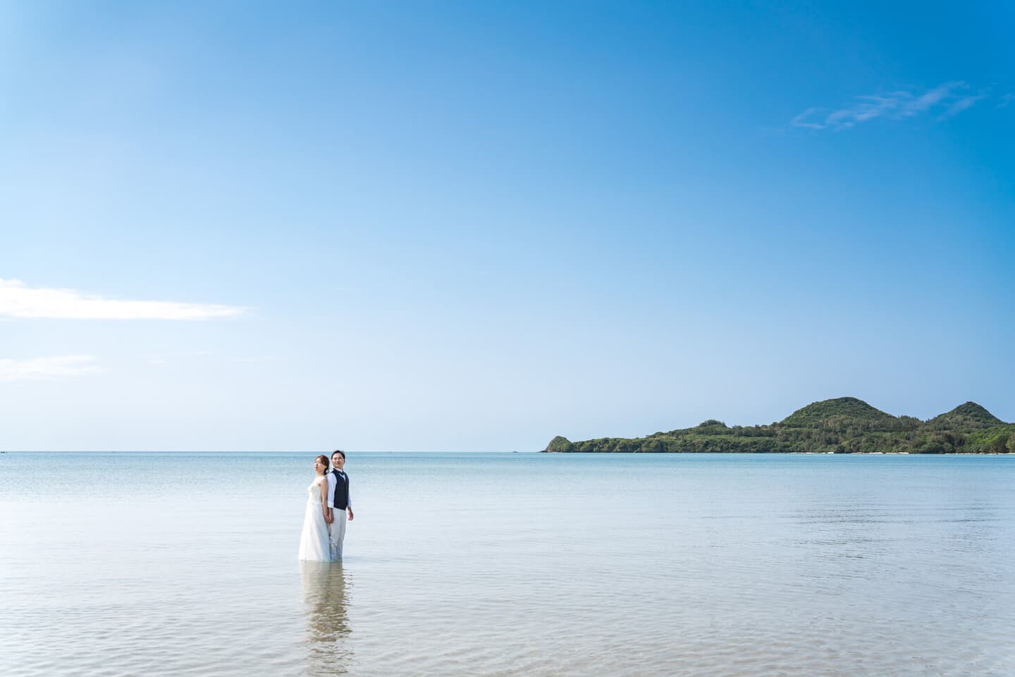 底地ビーチの海に入って背中合わせに立つ新郎新婦