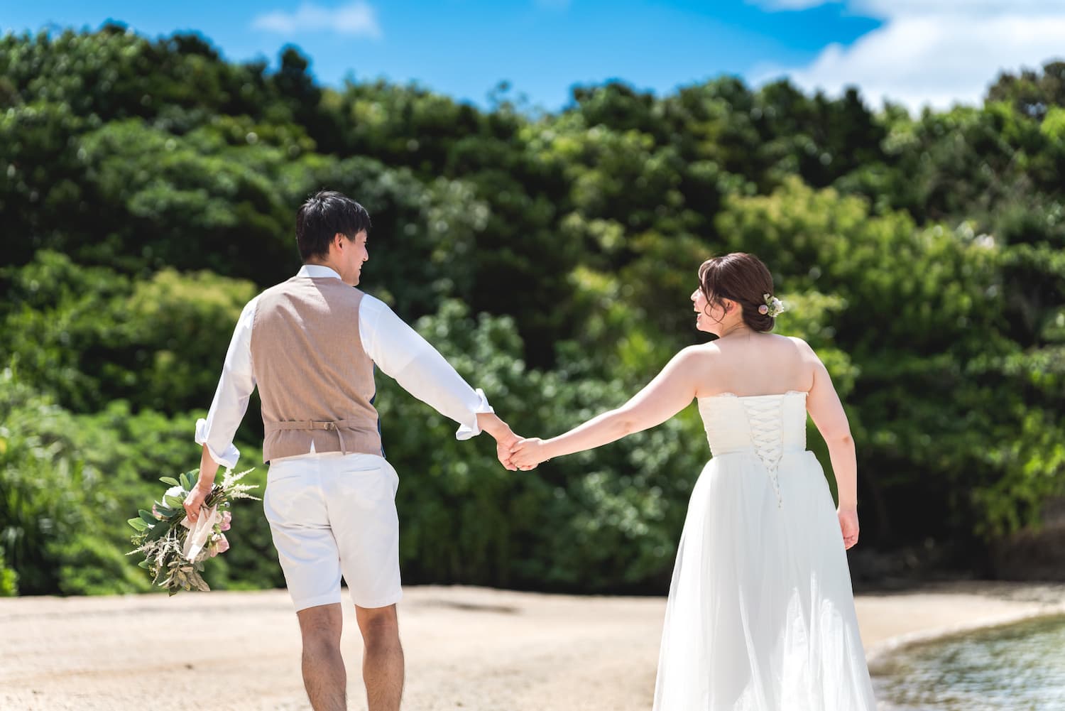 ビーチで手を繋いで歩く新郎新婦の後ろ姿