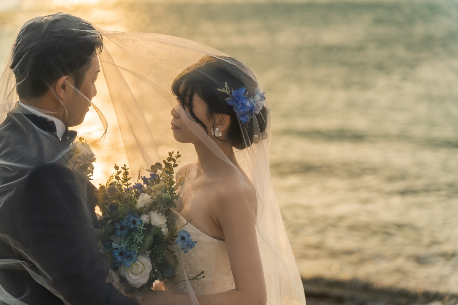 夕焼けに染まる海を背景にベールの中で見つめ合う新郎新婦