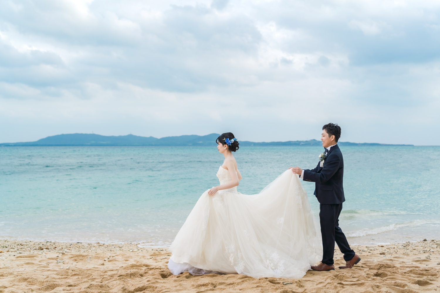 石垣島の海を背景に新婦のドレスを持って歩く新郎