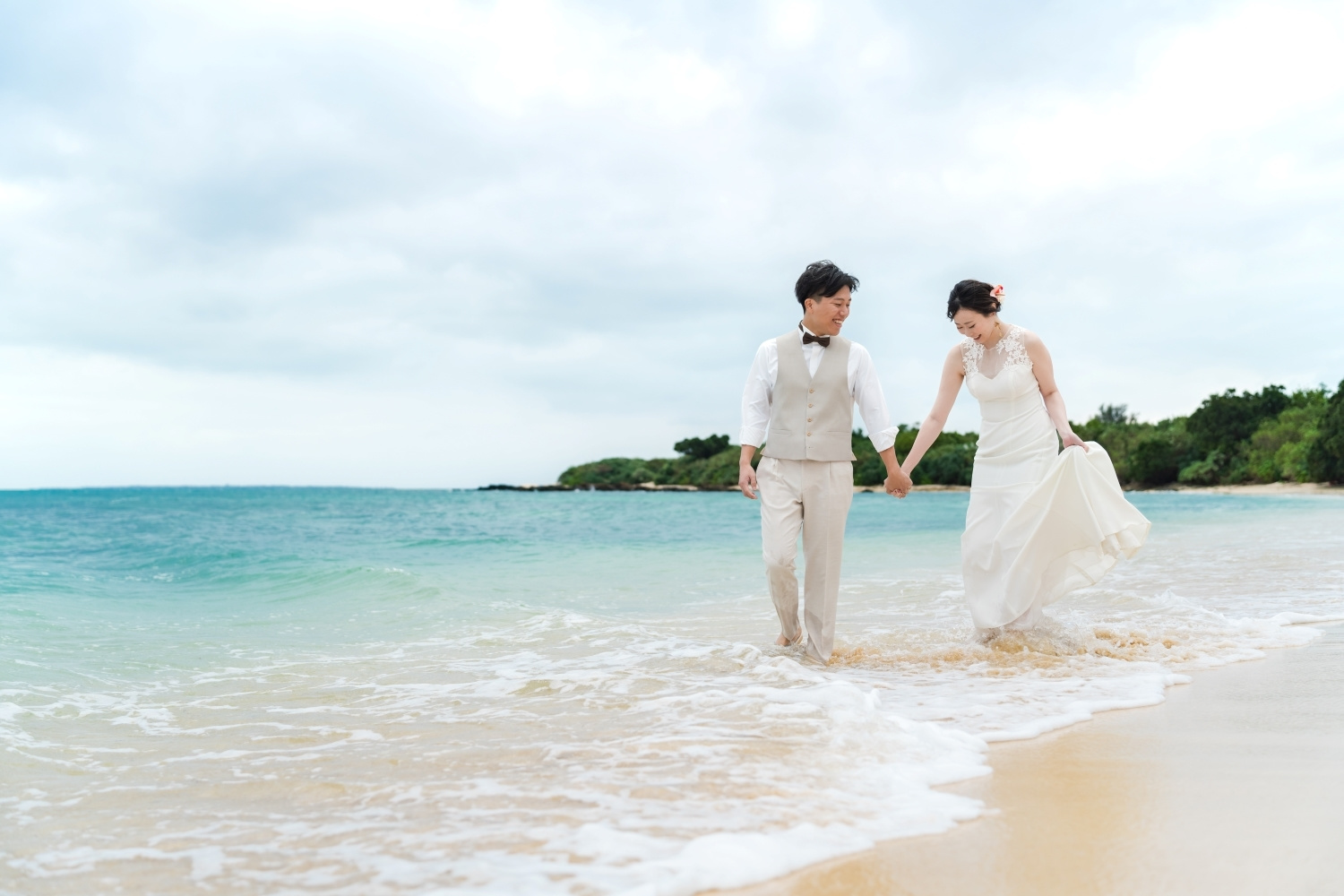 波打ち際で手を繋いで歩く新郎新婦